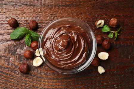 Chocolate hazelnut spread in bowl, nuts and mint on wooden table, flat layの写真素材