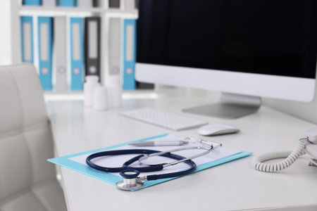 Clipboard, pen, computer and stethoscope on desk in doctor's office, closeupの写真素材
