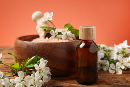 Spa composition with sea salt, bottle of cosmetic product and beautiful flowers on wooden table against coral background, closeupの写真素材