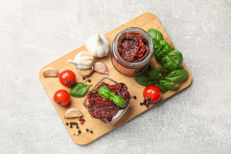 Delicious sun dried tomatoes, fresh vegetables, basil and garlic on light grey table, top view