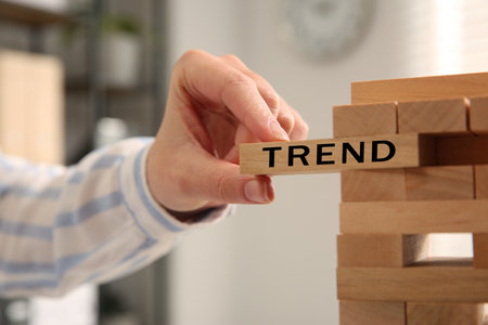 Woman removing wooden block with word Trend from tower indoors, closeupの写真素材