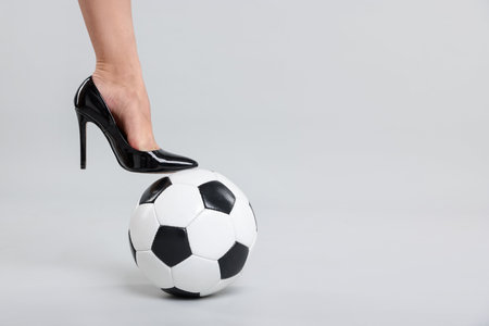 Woman in high heeled shoe with soccer ball on light background, closeup. Space for textの写真素材