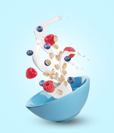 Oat flakes with fresh berries and milk splashing out from bowl in air on light blue backgroundの写真素材