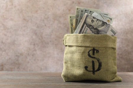 Bag with dollar banknotes on wooden table, space for text