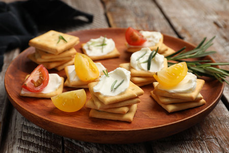 Tasty crackers with cream cheese, rosemary and tomatoes on wooden table, closeupの写真素材