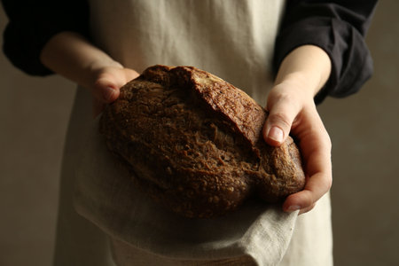 Woman with fresh loaf of bread on grey background, closeup