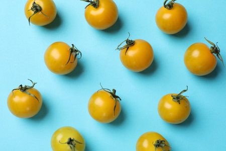 Ripe yellow cherry tomatoes on light blue background, flat lay