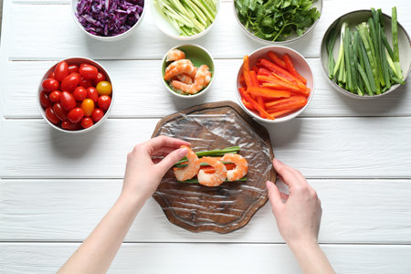 Woman making tasty spring roll at white wooden table, top viewの写真素材