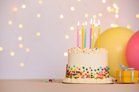 Tasty bento cake with colorful sprinkles, burning candles and other festive decor on table against light background, space for text. Bokeh effectの写真素材