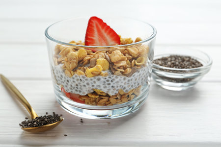 Delicious dessert with chia seeds, yogurt, granola and strawberries in glass on white wooden table, closeup. Superfoodの写真素材
