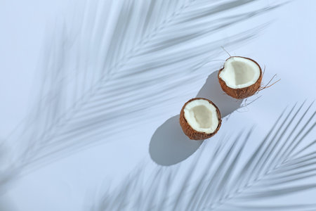 Fresh coconut and shadow cast by tropical palm on light grey background, top view. Space for textの写真素材