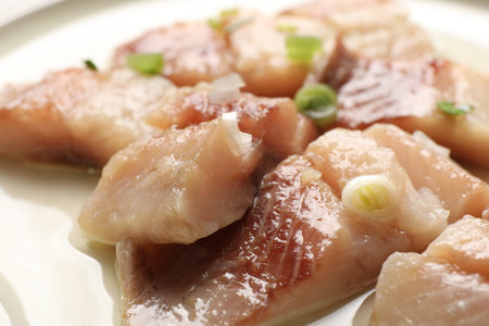 Pieces of delicious herring with green onions on plate, closeup