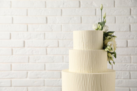 Delicious wedding cake decorated with flowers near white brick wall, closeup. Space for textの写真素材