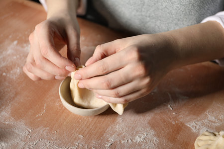 Woman making khinkali on table in kitchen, closeup