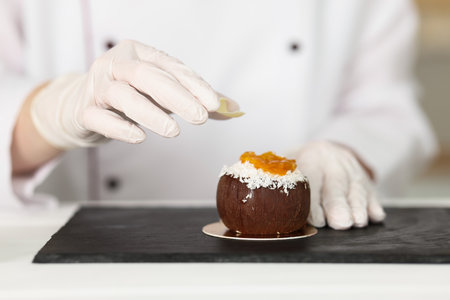 Confectioner decorating tasty dessert at white wooden table in kitchen, closeupの写真素材