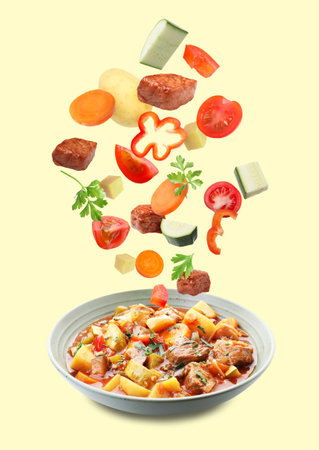 Delicious cooked stew. Fresh ingredients falling into bowl on beige backgroundの写真素材