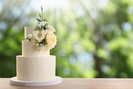 Beautiful wedding cake with floral decor on wooden table outdoors. Space for textの写真素材
