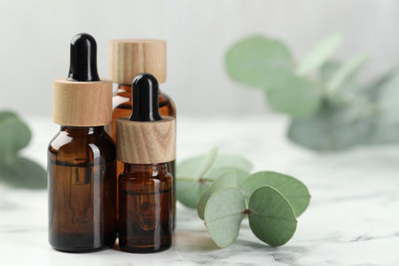 Bottles of essential oil and eucalyptus leaves on white marble table, closeupの写真素材