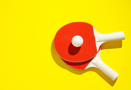 Ping pong rackets and ball on yellow background, top view. Space for textの写真素材