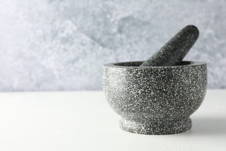 Stone mortar and pestle on white table, closeup. Space for text
