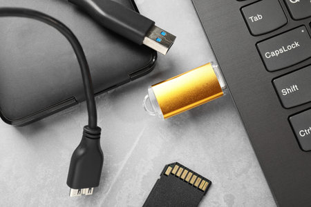 Flash drive connected to laptop, SD memory card and external hard disk on gray textured table, flat...