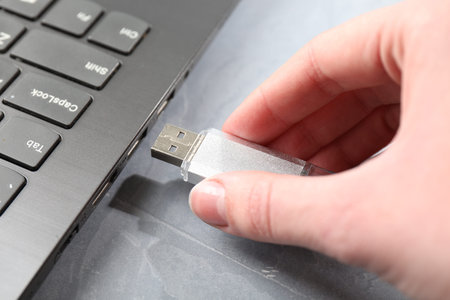 Woman inserting flash drive into laptop at gray textured table, closeup