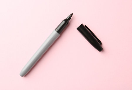 One black marker on light pink background, top view