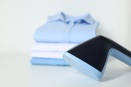 Upright steamer and stack of folded shirts on white table, closeupの写真素材