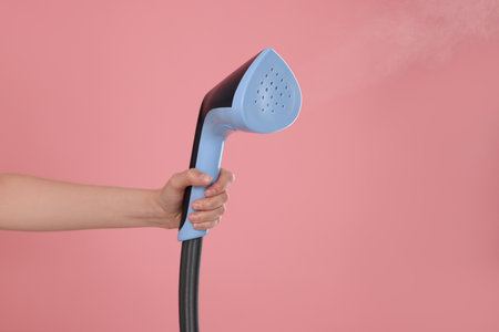 Woman with clothes steamer on pink background, closeup. Space for textの写真素材