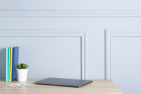 Laptop, stationery and floral decor on wooden office table near light wallの写真素材