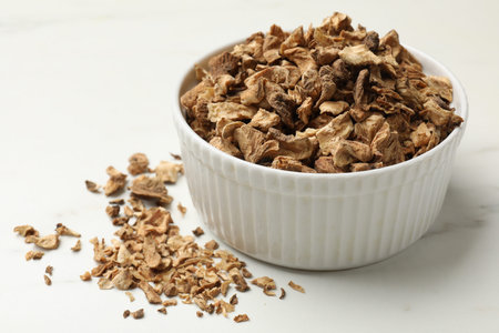 Pieces of dry chicory roots in bowl on white table, closeup