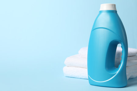 Bottle of fabric softener and towels on light blue background, space for textの写真素材