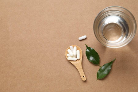 Collagen capsules, water and leaves on beige background, flat lay. Space for textの写真素材
