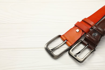 Two leather belts on white wooden table, above view. Space for textの写真素材