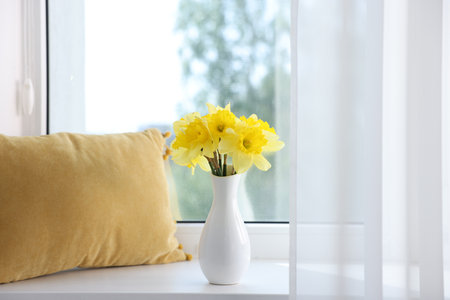 Beautiful daffodils in vase on windowsill at homeの写真素材
