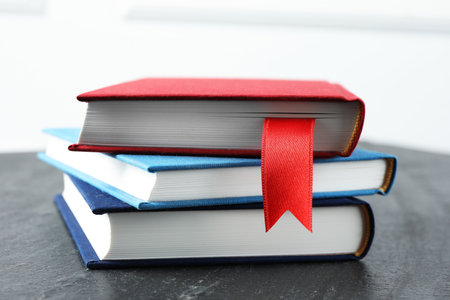 Book with red ribbon bookmark and colorful ones on dark textured table against light background, closeupの写真素材