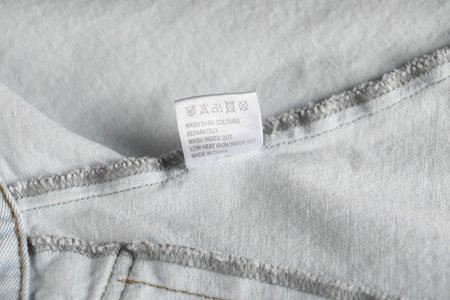 Clothing label with care symbols on garment as background, closeup
