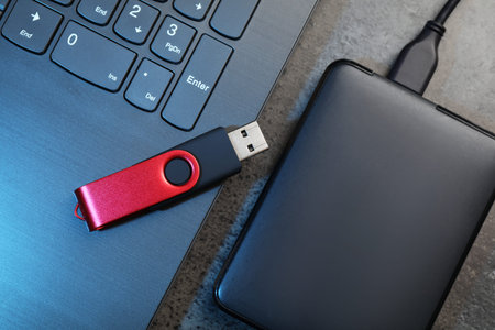 USB flash drive, hard disk drive with cable and laptop on dark grey table, flat lay