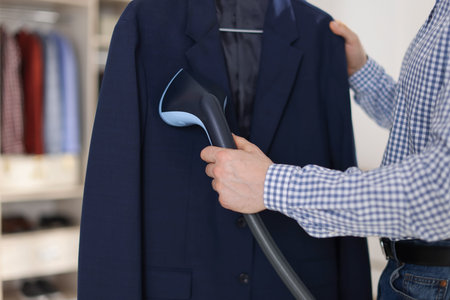 Man steaming jacket with stand steamer indoors, closeupの写真素材