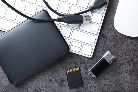 SD memory card, USB flash drive, hard disk drive with cable and keyboard on dark grey table, flat...