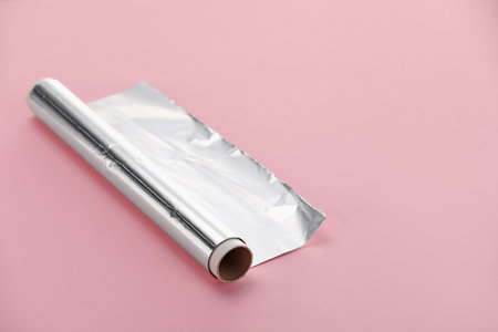 Roll of aluminum foil on pink background, closeup. Space for textの写真素材