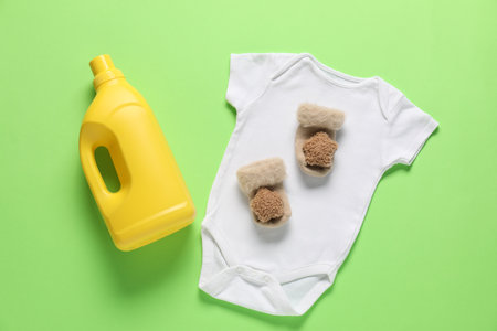 Bottle of fabric softener and baby clothes on green background, flat layの写真素材