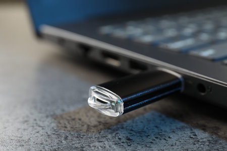 USB flash drive connected to laptop on dark grey table, closeup
