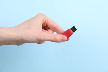 Woman holding USB flash drive on light blue background, closeup