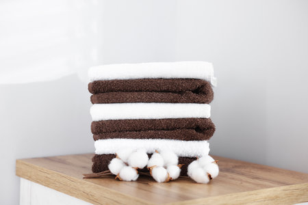 Stack of clean towels and cotton flowers on wooden cabinet indoorsの写真素材