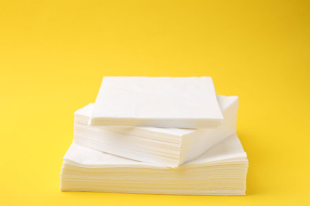 Stack of white handkerchiefs on yellow background, closeup