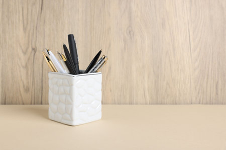 Ballpoint pens in holder on beige table against wooden background. Space for textの写真素材