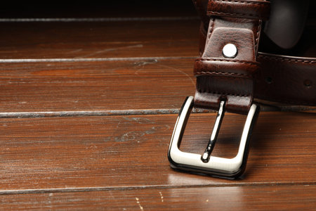 One brown leather belt on wooden table, closeup. Space for text