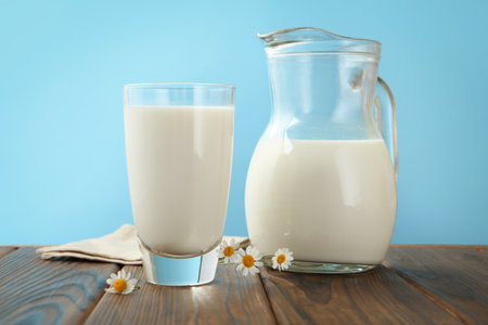 Fresh milk and flowers on wooden table against light blue background, closeupの写真素材