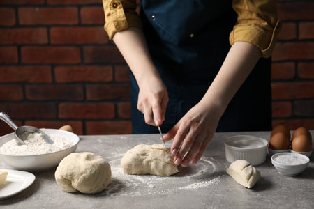 Woman cutting raw dough at light grey table, closeup